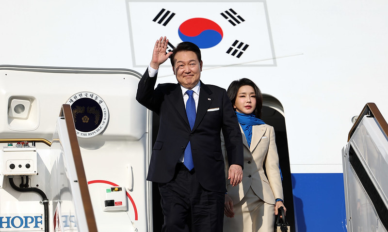 Former South Korean president, Yoon Suk Yul waving at the crowd while deboarding airplane with former first lady Kim Geon-hee behind him